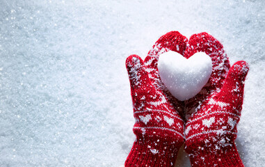 female hands in knitted mittens with snowy heart against snow background