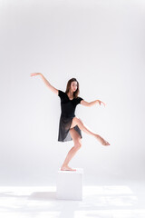 Canvas Print - A slender girl in a black sports dress poses while dancing on a white isolated background. Girl athlete dancing on a white isolated background with place for text or logo.