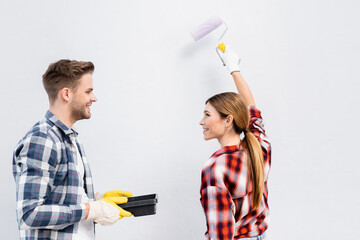 Canvas Print - smiling young woman with paint roller looking at man holding tray isolated on grey