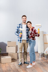 Wall Mural - full length of happy young couple hugging while holding paint rollers near cardboard boxes at home