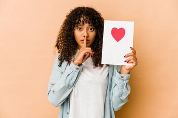 Wall Mural - Young african american afro woman holding a valentines day card keeping a secret or asking for silence.