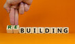 Rebuilding symbol. Male hand turns wooden cubes and changes words 'building' to 'rebuilding'. Business and rebuilding concept. Beautiful orange background, copy space.