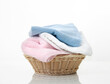 Folded towels stack in basket on white background,heap of colorful laundry on table.