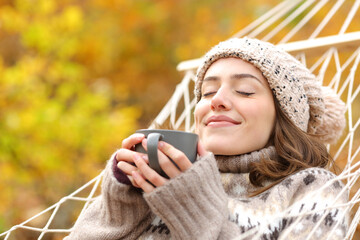 Wall Mural - Relaxed woman smelling coffee on hammock in autumn