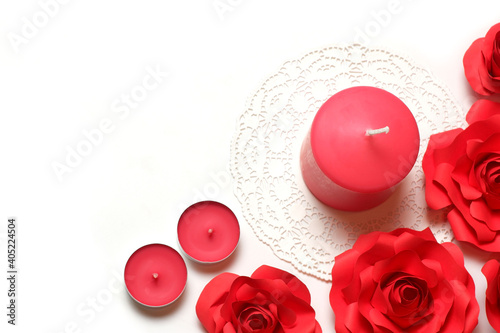 Few pink aromatic candles on white openwork paper napkin and few red handmade paper roses on white background top closeup view isolated. Love, rendezvous, relations, date, dating concept 