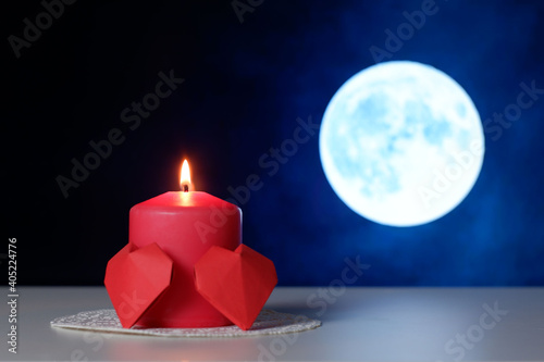 Couple of 3D red paper hearts, burning pink candle on white openwork paper napkin, full moon background closeup view selective focus. Love, Valentine's, women's day, relations, romantic concept 