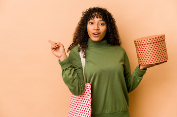 Wall Mural - Young african american afro woman holding a valentines day gift pointing to the side