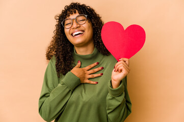 Wall Mural - Young african american afro woman holding a valentines day heart laughs out loudly keeping hand on chest.