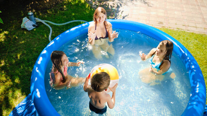 Happy laughing children with mother having fun and playing with inflatable ball in swimming yard. Family summer vacation and holidays