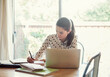 © LOUIS CHRISTIAN/Westend61 - Businesswoman using laptop while writing in book at office