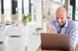 © Jo Kirchherr/Westend61 - Excited businessman showing winning gesture while working on laptop at home