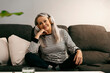 © Eloisa Ramos/Westend61 - Senior woman wearing headphones smiling while sitting with hand on chin at home