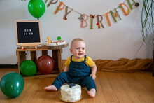 Smiling Baby Boy Sitting With Cake On Floor Against Decoration At Home