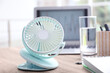 © New Africa - Modern portable fan on wooden table in office. Summer heat