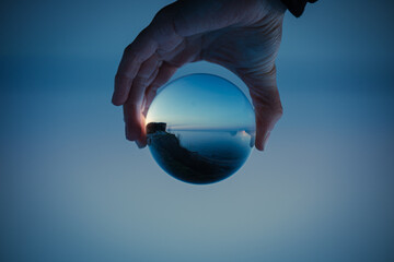 blue sky with a clear lake in crystal glass ball holding in hand