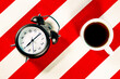 © Eloisa Ramos/Westend61 - Mug of coffee and alarm clock on white and red striped pattern