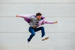 © Miguel Frias/Westend61 - Carefree young man with arms outstretched jumping against gray wall