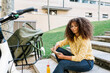 © Xavier Lorenzo/Westend61 - Young woman holding book while sitting by bicycle on steps