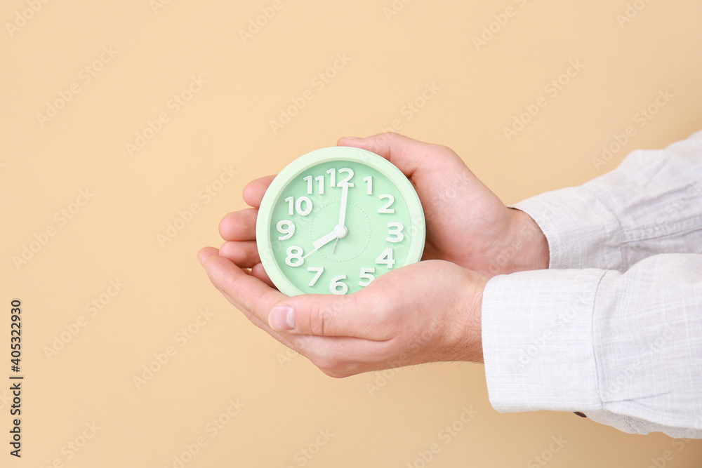 Male hands with alarm clock on color background