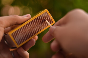 Canvas Print - Closeup shot of hands lighting matchstick on matchbox against a green bokeh background