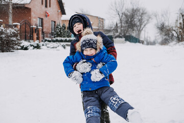 Outdoor winter activities for kids. Kids playing in the suburbs, winter backyard gathering. Boys having fun with snow