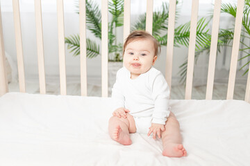 happy baby sitting in a crib in a white bodysuit