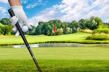 Wall Mural - Close-up of a hand wearing a golf glove holding a golf ball and a golf club between the fingers.