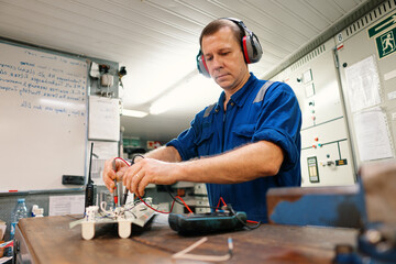 Marine electrical engineer officer in engine control room ECR. He works in workshop with electric equipment