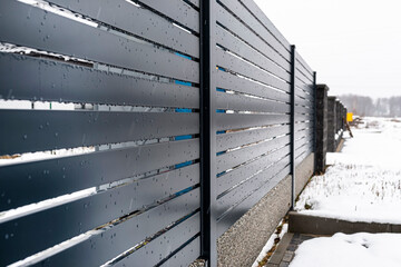 Wall Mural - Modern anthracite panel fencing, with a visible fence foundation connector, it rains in winter, in the background there is snow lying on the ground.