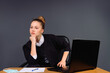 © Viorel - Pensive business woman in the office at the table with a computer and documents looks into the distance. Grey background.