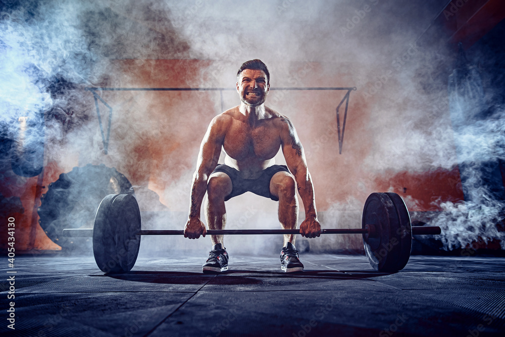 Muscular fitness man doing deadlift a barbell over his head in modern fitness center. Functional training. Snatch exercise. Smoke on background. - obrazy, fototapety, plakaty 