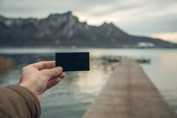 blank business card for your text and logo on the background of the Austrian mountain lake. black blank business card. black sheet of cardboard in hand and free standing