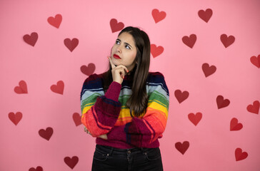 Young beautiful woman over pink background thinking about question with hand on chin, thoughtful about confusing idea with harts