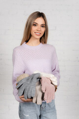 Sticker - Smiling woman holding basket with yarn and warm gloves near white brick wall