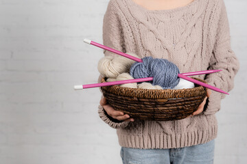 Canvas Print - Cropped view of basket with woolen yarn balls and needles in hands of woman in sweater on white background