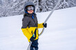 © Elena - A boy lifting on the ski drag lift rope in bright sport outfit on the ski resort mountain do a ski lesson during a snowfall. Ski resort in french mountain. Soft focus background. High quality photo