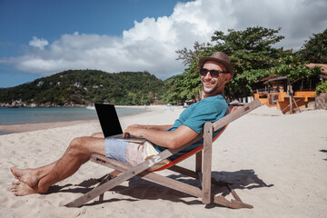 Wall Mural - attractive young man with laptop working on the beach. freedom, remote work, freelancer, technology,