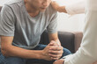 © KMPZZZ - Young asian man, male suffers from a mental who needs to therapy with a psychologist while sitting on couch to consult, psychiatrist has encouragement the patient by touching to make his feel relaxed.
