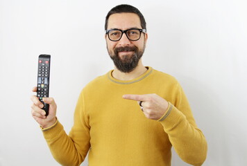 bearded man with eyeglasses smiling on white background points with his finger at the remote control he is holding in his hand