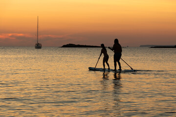 Wall Mural - Two people on the same board of paddle surf at sunset