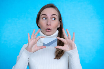 Photo portrait of excited girl holding bank card with two hands isolated on blue colored background