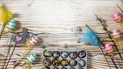 Wall Mural - Easter frame from decorative painted eggs, sprigs of greenery, pussy willow, Easter souvenirs, feathers, quail eggs on a wooden background. Easter composition top view, flat lay, copy space