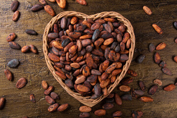 Raw cocoa beans in heart shaped basket with rustic background top view