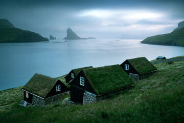 Wall Mural - Picturesque view of tradicional faroese grass-covered houses in the village Bour. Drangarnir and Tindholmur sea stacks on background. Vagar island, Faroe Islands, Denmark. Landscape photography