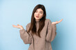 © luismolinero - Young Ukrainian teenager girl wearing a sweater over isolated blue background having doubts while raising hands