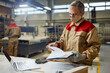 © Drazen - Male carpenter wearing face mask while going through paperwork in a workshop.