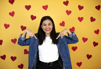 Young caucasian woman over yellow background with red hearts looking confident with smile on face, pointing oneself with fingers proud and happy.