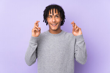 Young african american man isolated on purple background with fingers crossing