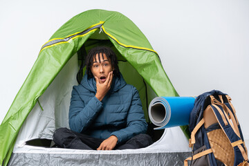 Sticker - Young african american man inside a camping green tent surprised and shocked while looking right