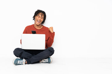 Sticker - Young african american man sitting on the floor and working with his laptop with phone in victory position